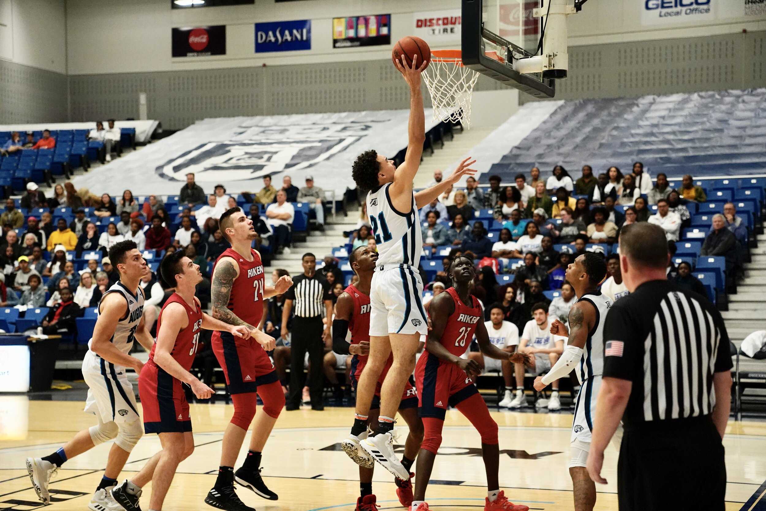 Troy Cracknell shoots a three inside Christenberry Fieldhouse during the 2019-20 season. At the top of the page, Troy Cracknell goes through player intros. (Photos taken by Carlos Rodriguez)